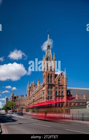 Movimento sfocato dell'autobus rosso di Londra fuori dalla stazione internazionale di St Pancras, catturando l'energia della città sotto un cielo blu brillante. Foto Stock