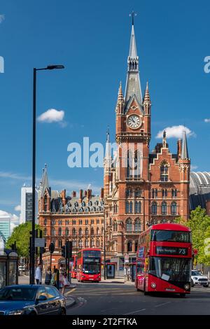 Autobus rossi e vita cittadina fuori St Pancras International, Londra, con la storica facciata in mattoni e cieli azzurri. Foto Stock