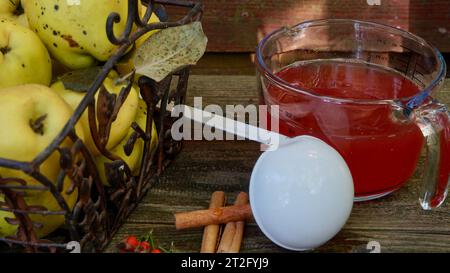 Un cestino pieno di quinces maturi, un mestolo, una brocca graduata piena di succo e bastoncini di cannella. Foto Stock