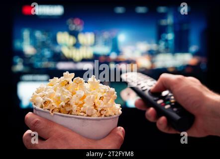 Serata di film in TV con la famiglia. Piattaforma di streaming VOD. Popcorn e telecomando. Intrattenimento video e snack. Riprodurre film online in televisione. Foto Stock