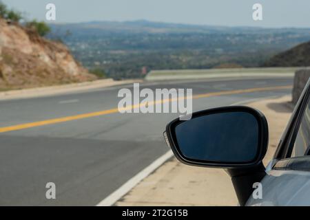 Concentratevi sullo specchio di un'auto, sullo sfondo potete vedere una strada di montagna. Foto Stock