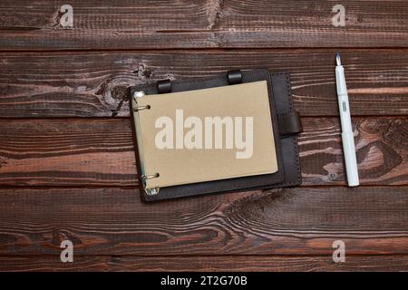 il taccuino con carta artigianale in forma dispiegata giace su una superficie di legno con una penna bianca Foto Stock