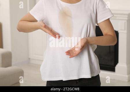 Donna che mostra macchie di caffè sulla camicia al chiuso, primo piano Foto Stock