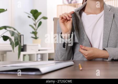 Donna che mostra macchie di caffè sulla giacca al tavolo di legno all'interno, primo piano Foto Stock