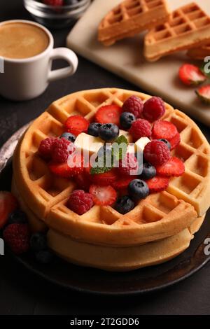 Gustosi waffle belgi con frutti di bosco freschi, formaggio e tazza di caffè sul tavolo nero Foto Stock