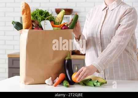 Donna e borsa di carta con diversi prodotti sul tavolo in cucina Foto Stock