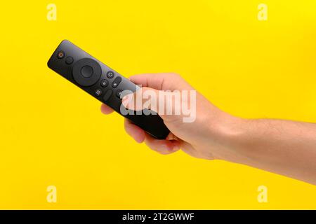 Lo sfondo giallo a mano tiene il telecomando del televisore premendo il pulsante con il dito Foto Stock
