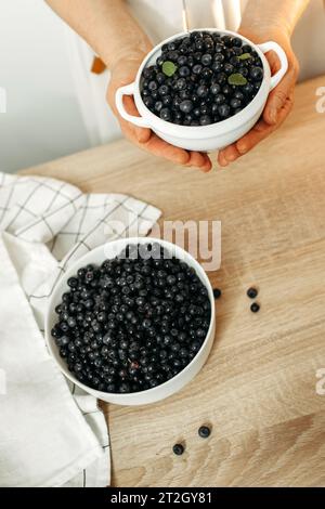 Ci sono piatti di mirtilli maturi sul tavolo della cucina e nelle mani dei donne. Prodotti biologici, vista dall'alto. Foto Stock