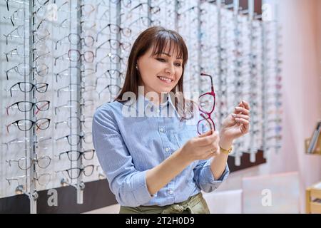 Donna in un negozio di ottica che acquista, sceglie montature per occhiali Foto Stock