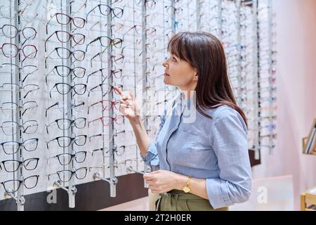 Donna in un negozio di ottica che acquista, sceglie montature per occhiali Foto Stock