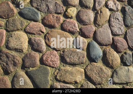 La struttura della strada in pietra, il marciapiede, le pareti di grandi pietre grigie antiche medievali rotonde, le pietre acciottolate. Lo sfondo. Foto Stock