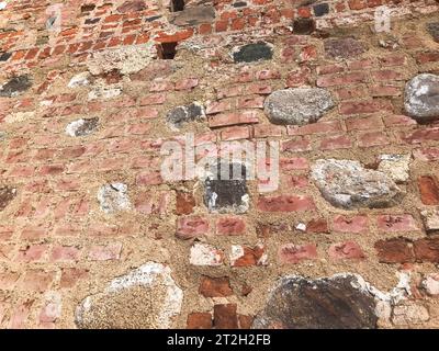 La consistenza dell'antica pietra medievale antica, il peeling duro, la parete di mattoni di argilla rossa rettangolare e grandi pietre, ciottoli. T Foto Stock