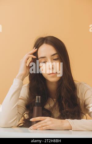 Bella donna che tiene una bottiglia di cosmetici isolata su sfondo beige. Foto Stock
