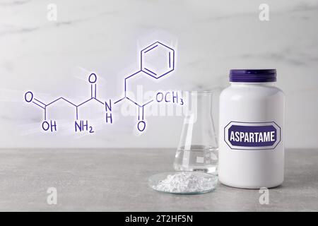 Formula chimica strutturale dell'aspartame. Dolcificante artificiale in petri e bottiglia su tavolo grigio Foto Stock