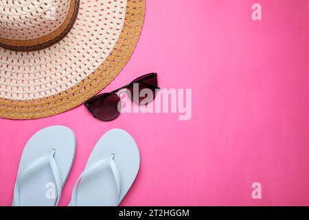 Cappello di paglia, eleganti occhiali da sole e infradito su sfondo rosa, piatto con spazio per il testo. Accessori per la spiaggia Foto Stock