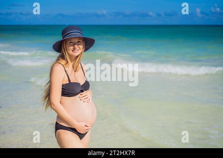 Radiosa donna incinta in costume da bagno, sullo sfondo mozzafiato di un mare turchese. Bellezza serena della maternità vicino alla riva Foto Stock