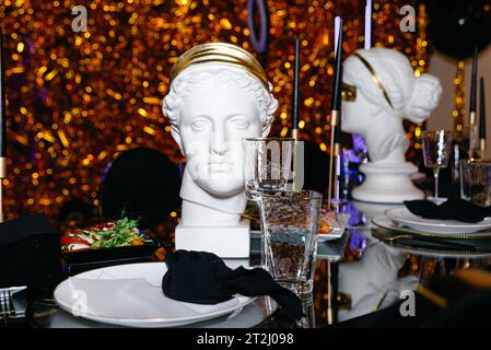 Tavolo di lusso per matrimoni o altre cene con servizio catering. Scultura della testa come decorazione su uno sfondo dorato. Foto Stock