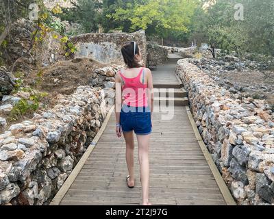 Una ragazza sale i gradini di una scala di legno in una zona rocciosa di montagna, una turista eco-trail in una calda località tropicale del sud della campagna orientale. Foto Stock