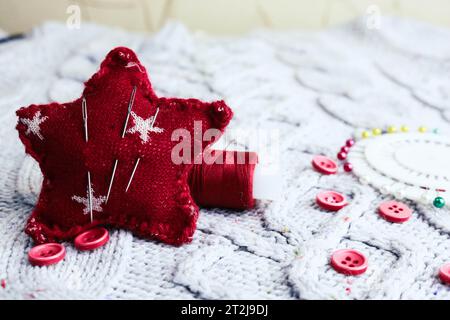 Splendida consistenza di un morbido maglione naturale caldo, tessuti con motivo a maglia e piccoli bottoni rotondi rossi per cucire e uno spiedino di filo e ago Foto Stock