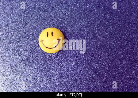 Giocattolo rotondo sorridente sorridente di plastica giallo Emoji con faccia rotonda su sfondo blu. Foto Stock