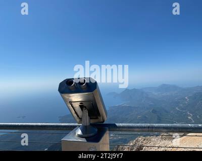 Binocolo stazionario grigio metallo sulla piattaforma di osservazione con vista sul mare, sulle montagne e sulla città. Paesaggio marino dall'alta riva. Foto Stock