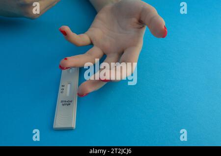 analisi del sangue per la diagnosi del coronavirus. una ragazza con una manicure rossa brillante ha una goccia di sangue sul dito anulare. analisi del sangue capillare da rilevare Foto Stock