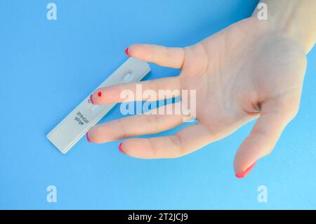 analisi del sangue per la diagnosi del coronavirus. una ragazza con una manicure rossa brillante ha una goccia di sangue sul dito anulare. puntura al dito lancetta, ra domestica Foto Stock