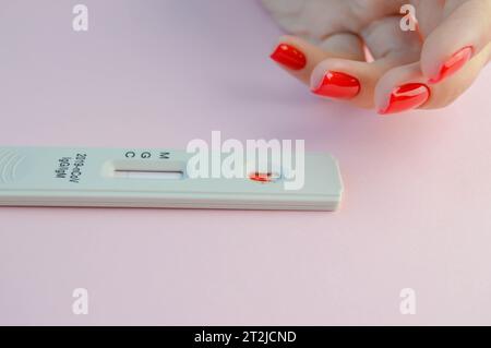 ragazza con una manicure rossa brillante che fa un test per il coronavirus. un esame del sangue per determinare il coronavirus a casa. la procedura si svolge su un elegante e. Foto Stock