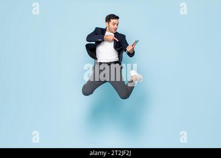 Eccitato manager maschio caucasico in abiti casual intelligenti che saltano e puntano lo schermo del tablet su sfondo blu Foto Stock