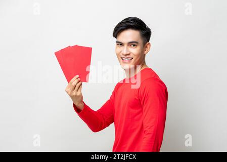 Sorridente bell'uomo asiatico che regge buste rosse o Ang Pow in studio sfondo grigio isolato per i concetti del capodanno cinese Foto Stock