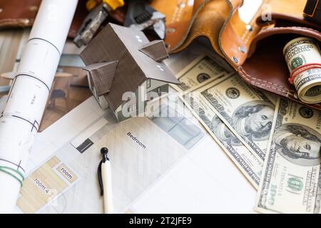 Piccola casa e il salvadanaio con pile di centinaia di fatture del dollaro isolato su uno sfondo bianco. Foto Stock