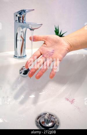 Primo piano di una donna irriconoscibile che si lava i glitter viola della mano in un lavandino del bagno Foto Stock
