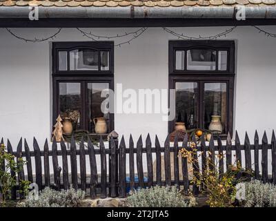 Vista frontale dettagliata di una tradizionale casa del villaggio con pareti bianche, finestre e recinzione in legno, vasi e piante come decorazione, Holloko, Ungheria, Pasqua Foto Stock