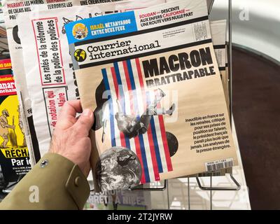 Londra, Regno Unito - 21 Apr 2023: A male Hand REACH for the latest issue of Courrier International magazine at a press kiosk, with the headline Macron Irrattrapable on its cover Foto Stock