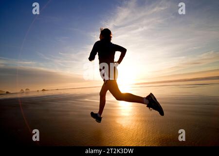 Una donna fa jogging lungo la sabbia bagnata durante un bellissimo tramonto. Foto Stock