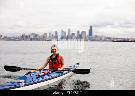 Una giovane ragazza canoa in una giornata nuvolosa nel Puget Sound al largo della costa del centro di Seattle. Foto Stock