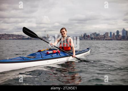 Una giovane ragazza canoa in una giornata nuvolosa nel Puget Sound al largo della costa del centro di Seattle. Foto Stock