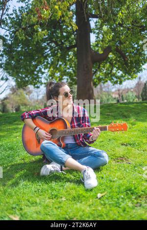 Vista frontale di una giovane donna hipster che indossa occhiali da sole, seduta Foto Stock