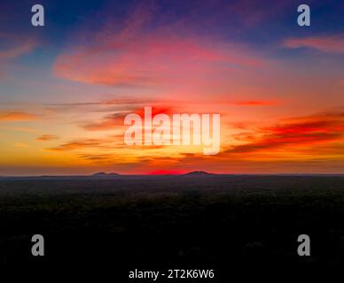 Un tramonto vibrante illumina il cielo e crea una silhouette sulle colline sullo sfondo Foto Stock
