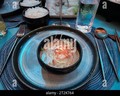 Vista dall'alto di una gustosa e piccante zuppa tailandese di pesce Tom Yum servita in una ciotola nera per cena. Foto Stock