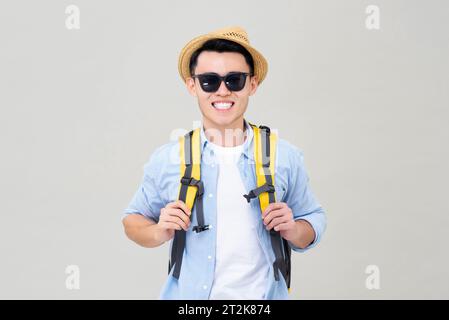 Porttrait di un giovane turista asiatico sorridente con zaino che indossa cappello e occhiali da sole, letto per le vacanze estive, studio girato isolato in uno zaino grigio Foto Stock