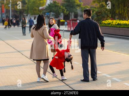 Una coppia vietnamita cammina con la loro giovane figlia che indossa un vestito rosso e indossa gli occhiali da sole a Ba Dinh Square, Hanoi, Vietnam. Foto Stock