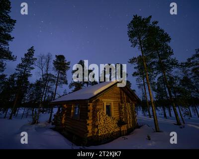 Paesaggio notturno con capanna in legno in una foresta finlandese Foto Stock