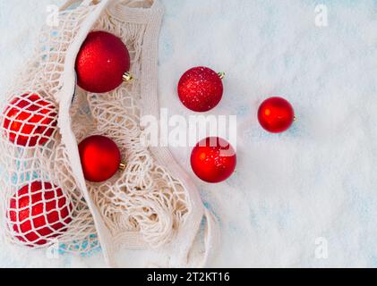 Composizione creativa composta da baule di Natale rosse che escono dal sacco a rete in rete su sfondo innevato. Stile minimalista per Natale o Capodanno. Idea invernale. Foto Stock