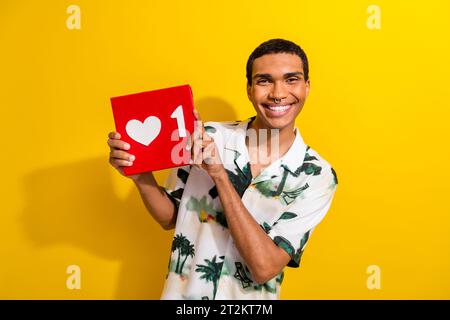 Foto di un uomo toothy con una camicia piercing vestita con stampa di palme che regge i social media come un'icona isolata su sfondo giallo Foto Stock