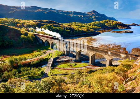 Treno a vapore giacobita e carrozze che attraversano il viadotto a 8 archi nan Uamh West Coast Scozia in autunno Foto Stock
