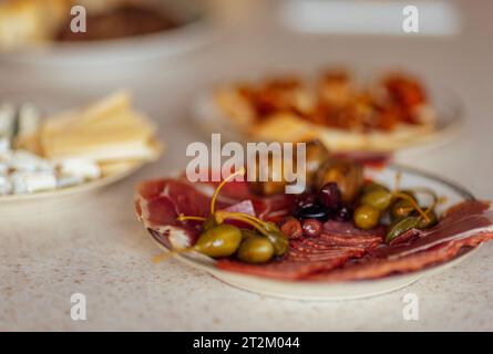 Primo piano di piatti con vari deliziosi spuntini su un tavolo in marmo bianco. Fette di prosciutto, salsicce, capperi e olive su un piatto in primo piano Foto Stock