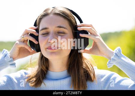 Ritratto di una giovane donna millenaria allegra ed elegante che indossa una giacca in denim all'aperto, ascolta musica con le cuffie, balla. Foto di alta qualità Foto Stock