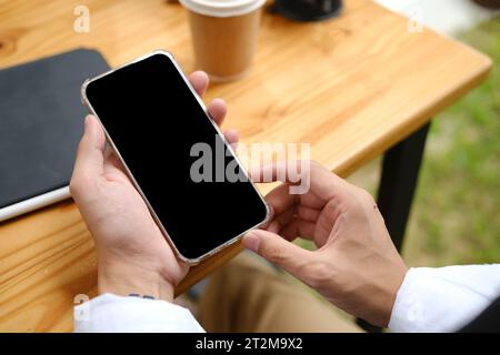 Colpo dall'alto, uomo d'affari che usa il suo cellulare, legge informazioni o e-mail sullo schermo del telefono alla sua scrivania. Mockup schermo nero del telefono.. Foto Stock