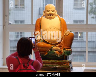 Una donna scatta una foto del Buddha di porcellana della dinastia Ming al British Museum di Londra, Regno Unito Foto Stock